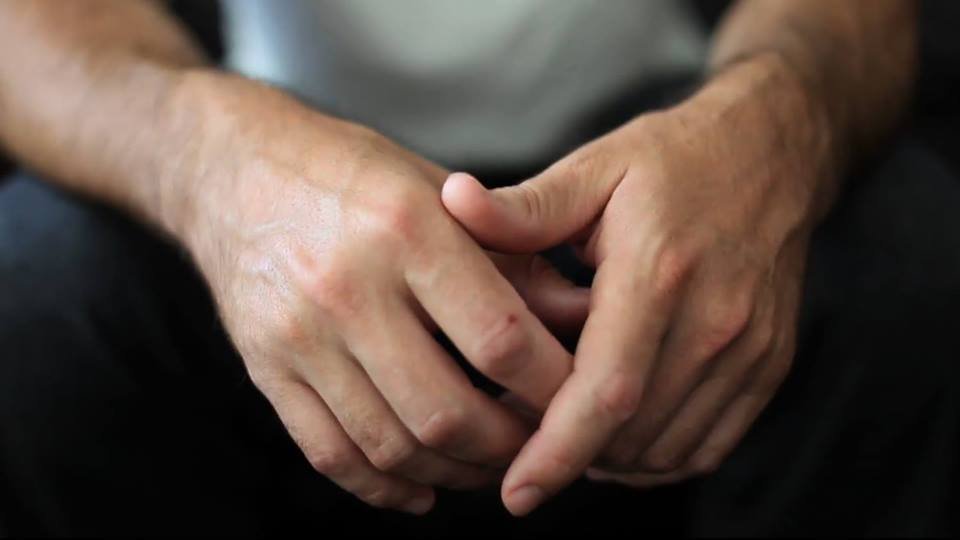 A close up image of hands resting in a lap in a forward position. The hands are presumed to be those of an anonymous white male. 