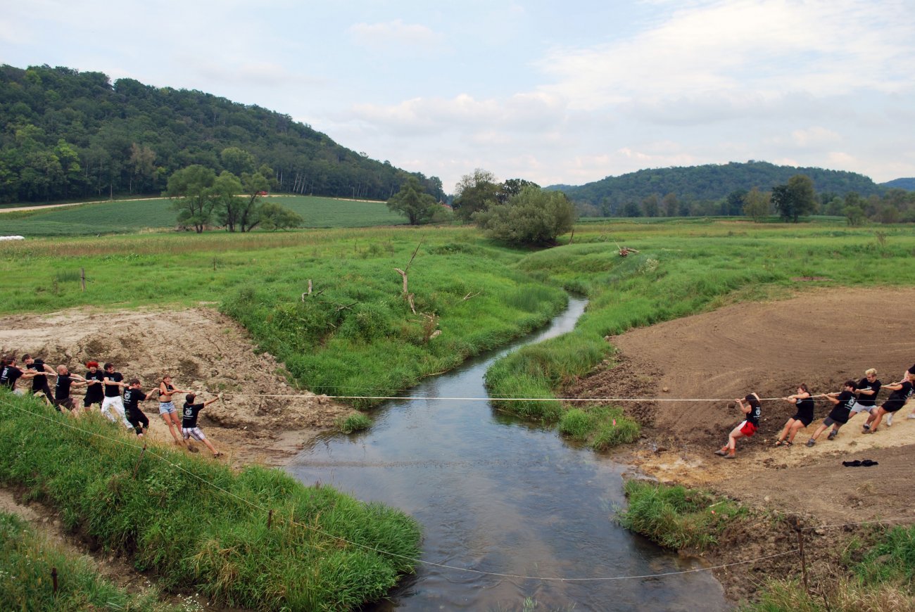 two groups of people playing tug of war across a stream