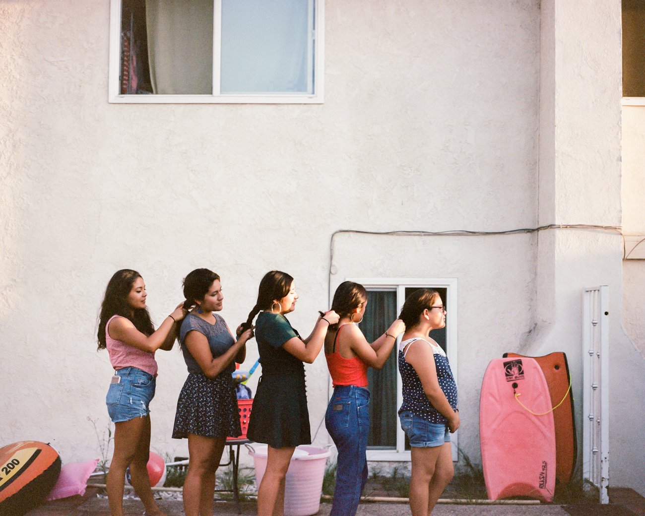 Image of a line of girls braiding each other’s hair. 