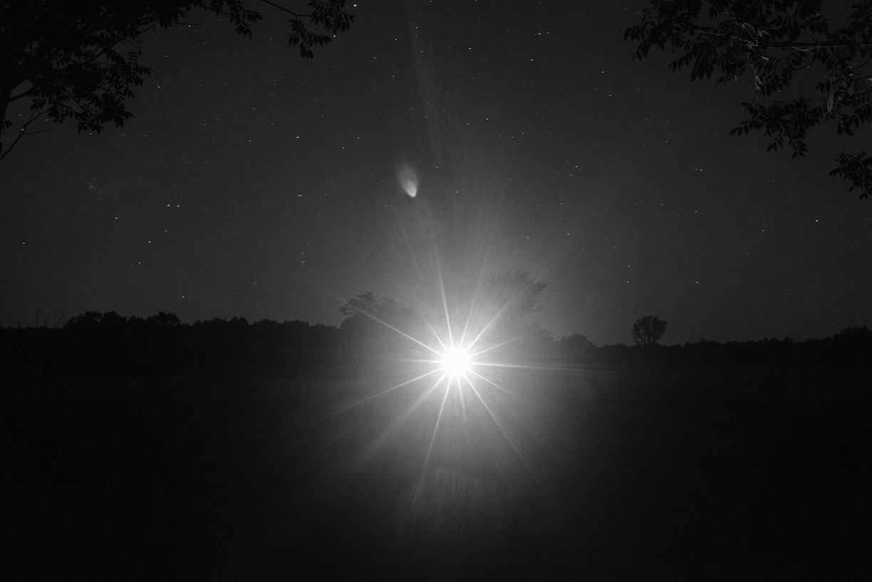 Black and white image of light flare in a dark landscape
