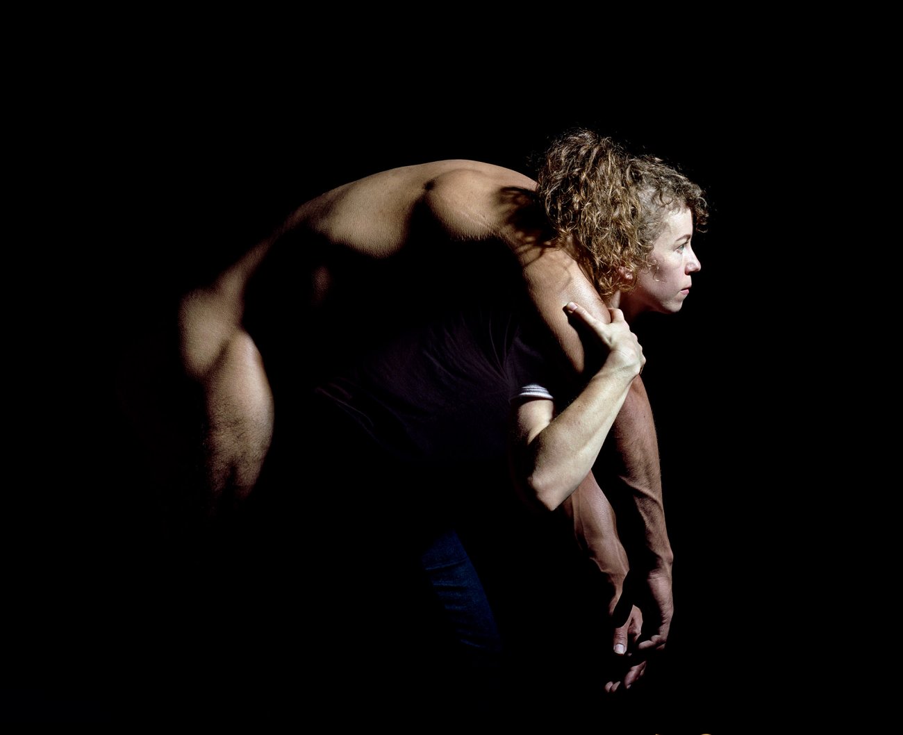 Color photograph of woman carrying a nude figure draped over her back