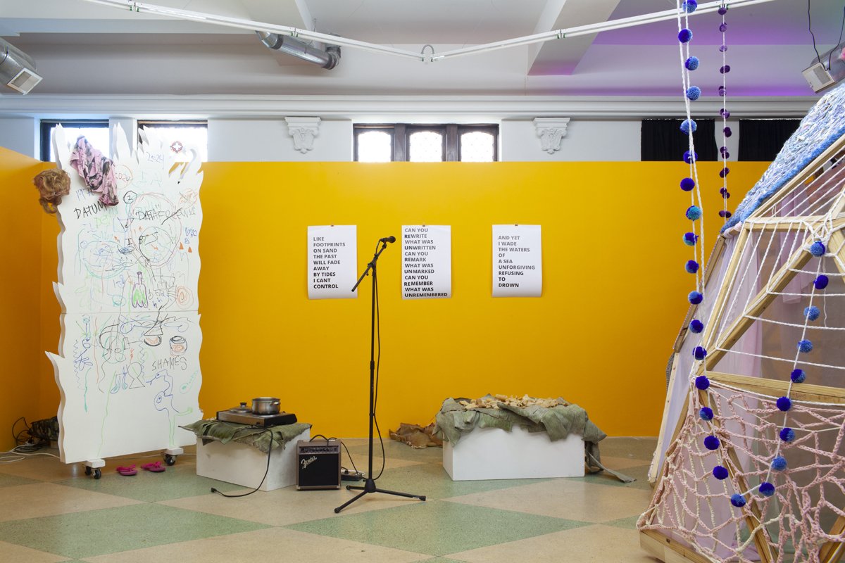 Installation image of exhibition with microphone and pa, crocheted dome, and white room divider with drawings in marker. 
