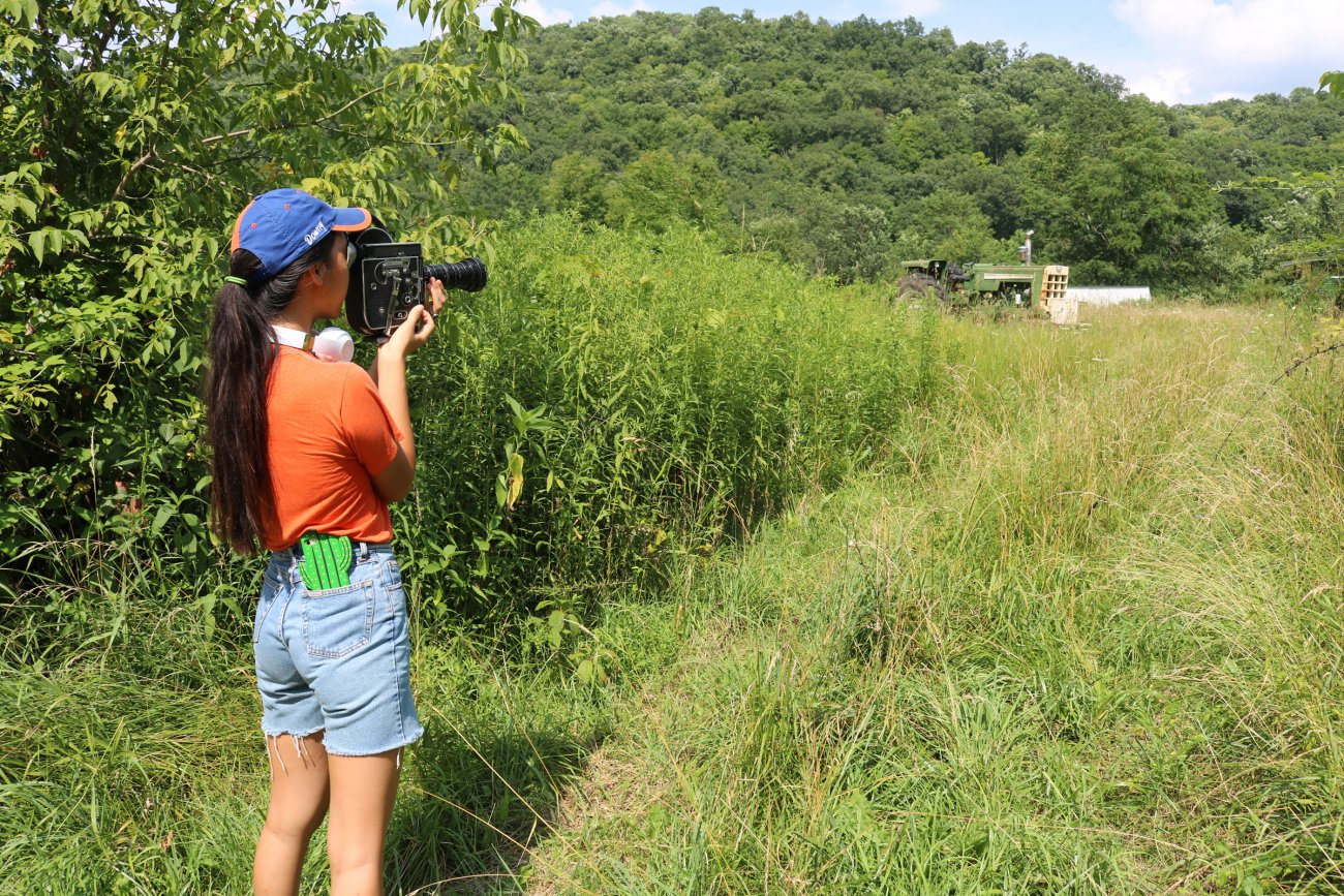 Artist using 16mm camera in grassy field 