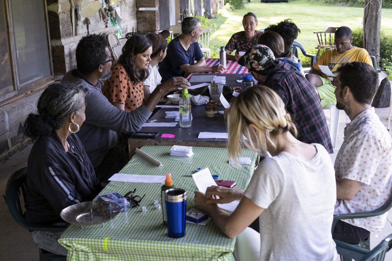 a group of artists gather at a picnic table with papers and other materials