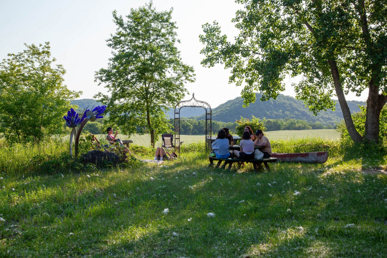 Group of artists sitting at picnic table in front of green sunlit field