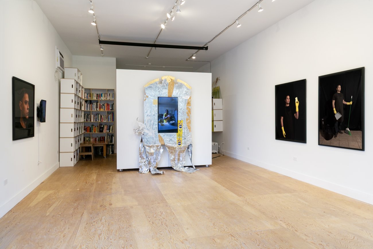 Exhibition installation with photographs of the artist on the left and right walls and a center altar with a monitor and mylar blankets.