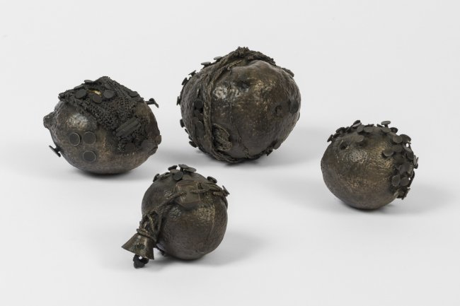 Photograph of four circular cast bronze objects with nails and other materials sticking out of them