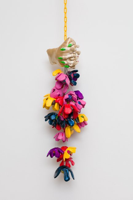 Photograph of a sculptural work by Frankie Toan, wilting flowers made of various fabrics and vinyl are held by two satin hands, hanging against a white wall.