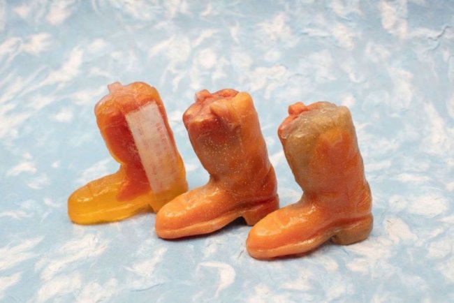 Photograph of three small orange boot sculptures on a white and blue backdrop
