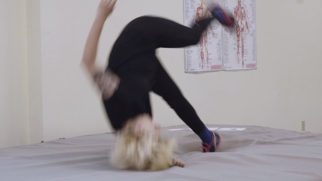 Still image from video work featuring a blurred figure upside down doing a front flip